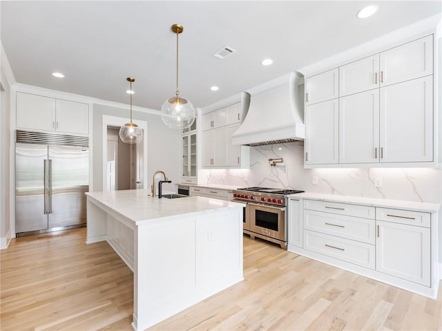 kitchen with pendant lighting, high quality appliances, white cabinetry, sink, and custom range hood