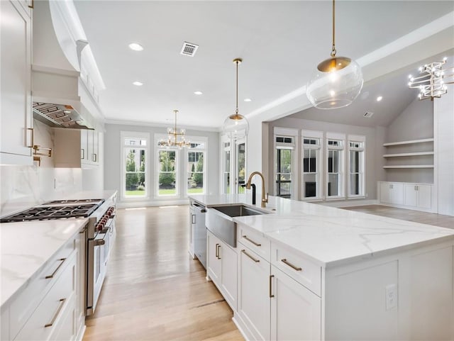 kitchen featuring white cabinetry, sink, decorative light fixtures, and an island with sink