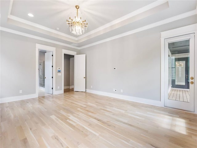 empty room with a chandelier, crown molding, a raised ceiling, and light wood-type flooring