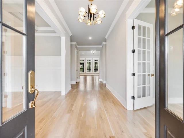 entrance foyer with crown molding, light wood-type flooring, a chandelier, and french doors