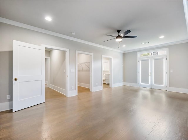 unfurnished bedroom with crown molding, a walk in closet, light hardwood / wood-style floors, and french doors