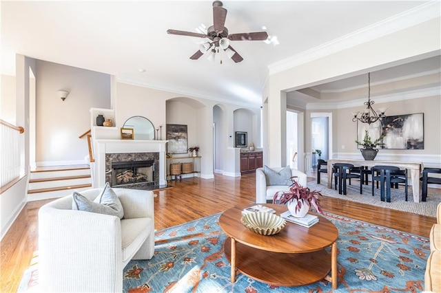 living room featuring crown molding, a high end fireplace, wood-type flooring, and ceiling fan with notable chandelier