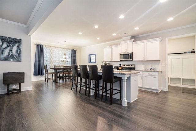 kitchen with light stone counters, a kitchen island with sink, a breakfast bar, white cabinets, and appliances with stainless steel finishes