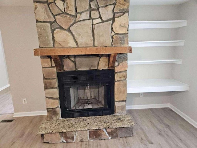 room details with baseboards, a stone fireplace, and wood finished floors