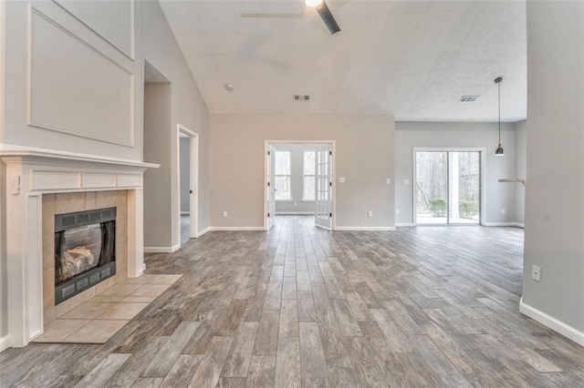 unfurnished living room featuring a tiled fireplace, plenty of natural light, light wood-type flooring, and ceiling fan