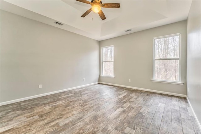 spare room featuring wood-type flooring, plenty of natural light, ceiling fan, and a tray ceiling