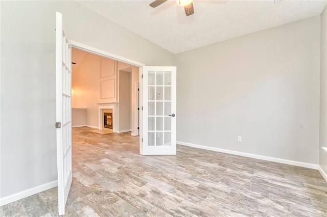 spare room with ceiling fan, light hardwood / wood-style flooring, french doors, and vaulted ceiling