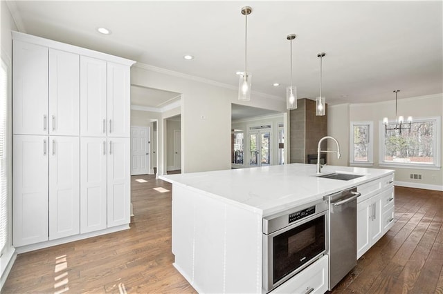 kitchen featuring sink, a kitchen island with sink, white cabinetry, hanging light fixtures, and stainless steel dishwasher