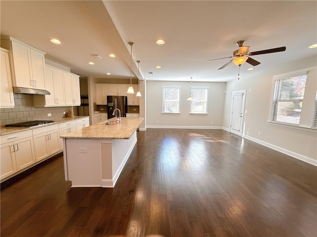 kitchen featuring a kitchen island with sink, under cabinet range hood, black appliances, white cabinetry, and a sink