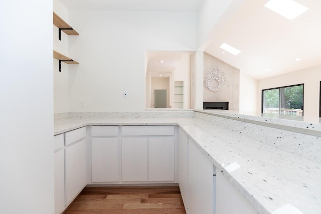 kitchen with white cabinets, lofted ceiling, light hardwood / wood-style floors, and light stone countertops