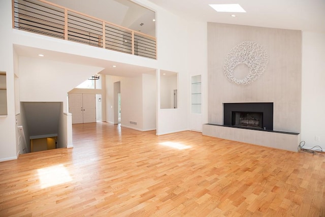 unfurnished living room with a high ceiling, built in shelves, and light wood-type flooring