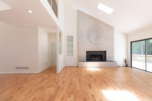 unfurnished living room featuring a skylight, light hardwood / wood-style floors, high vaulted ceiling, and a fireplace