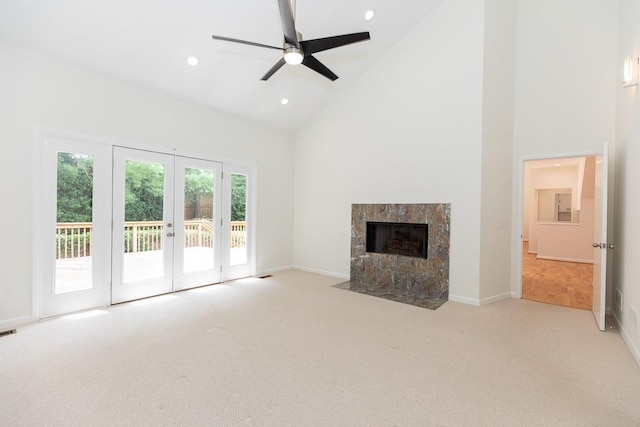 unfurnished living room with ceiling fan, high vaulted ceiling, light carpet, a tile fireplace, and french doors