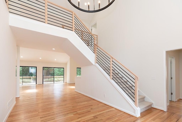 staircase featuring a chandelier, light hardwood / wood-style floors, and a towering ceiling