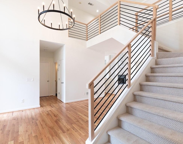 stairway featuring light hardwood / wood-style flooring, a towering ceiling, and an inviting chandelier