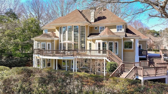 rear view of house with a shingled roof, stairway, a deck, and stucco siding