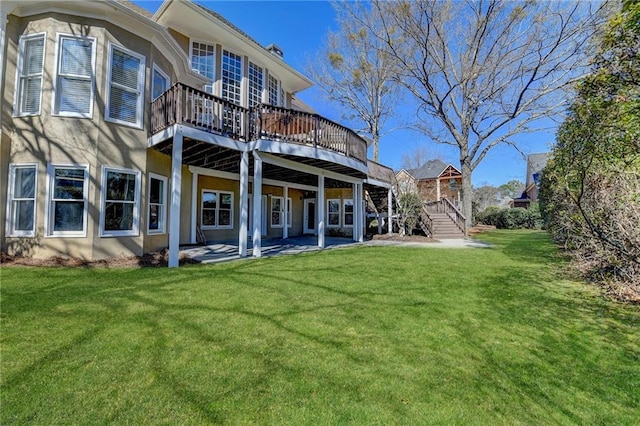 rear view of property with stucco siding, a lawn, a patio area, a wooden deck, and stairs