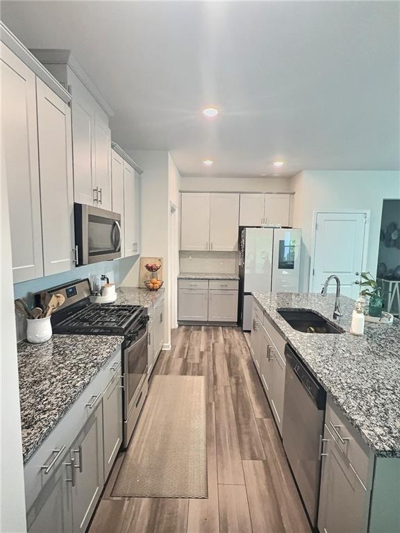 283 Wells Cir, Canton, GA 30114 - kitchen featuring stainless steel appliances, a sink, wood finished floors, light stone countertops, and an island with sink