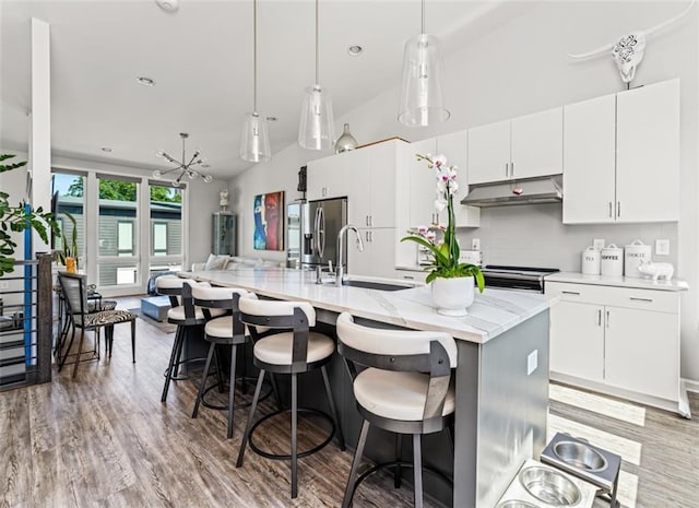 kitchen featuring white cabinetry, stainless steel fridge, a center island with sink, and pendant lighting