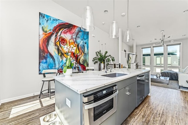 kitchen with stainless steel appliances, gray cabinetry, open floor plan, a kitchen island with sink, and a sink