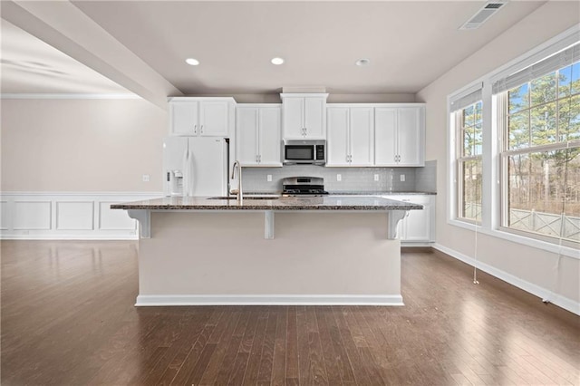 kitchen with visible vents, a kitchen island with sink, appliances with stainless steel finishes, and dark stone counters