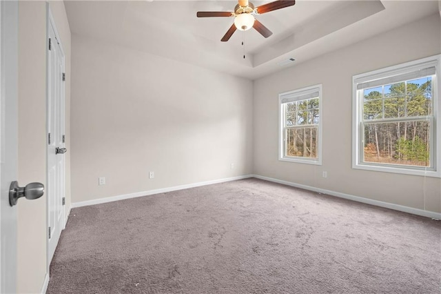 spare room featuring a tray ceiling, carpet, ceiling fan, and baseboards