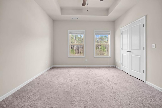 unfurnished bedroom featuring a raised ceiling, light colored carpet, visible vents, ceiling fan, and baseboards