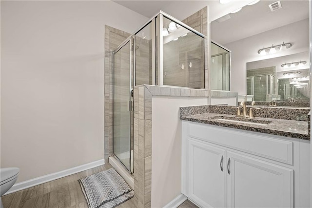 full bathroom featuring a stall shower, visible vents, toilet, wood finished floors, and vanity