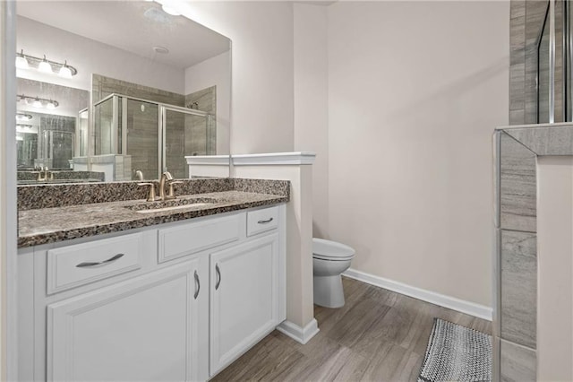 full bathroom with toilet, a stall shower, vanity, wood finished floors, and baseboards