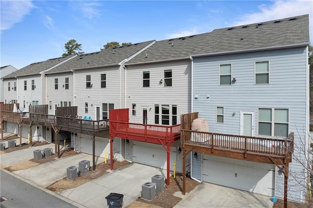 rear view of property with an attached garage, driveway, and cooling unit