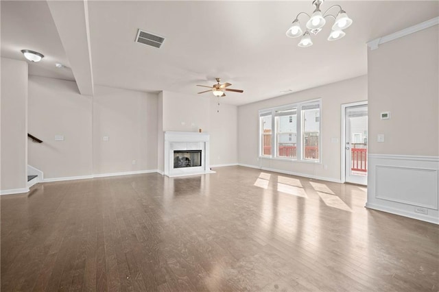 unfurnished living room with a fireplace, visible vents, stairway, wood finished floors, and ceiling fan with notable chandelier