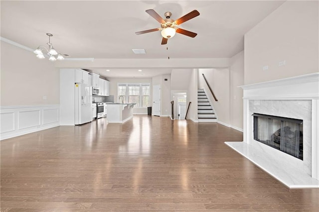 unfurnished living room featuring a decorative wall, ceiling fan with notable chandelier, a high end fireplace, stairs, and dark wood finished floors