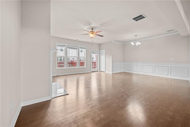 empty room featuring a decorative wall, ceiling fan with notable chandelier, wood finished floors, visible vents, and wainscoting