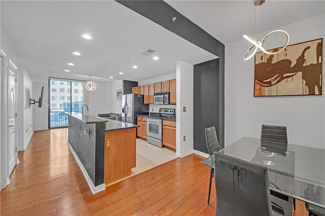 kitchen featuring a breakfast bar area, a center island with sink, light hardwood / wood-style flooring, appliances with stainless steel finishes, and pendant lighting