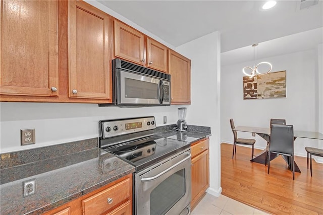 kitchen with stainless steel appliances, light wood-type flooring, hanging light fixtures, and dark stone counters