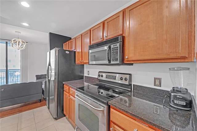 kitchen featuring appliances with stainless steel finishes, decorative light fixtures, dark stone countertops, light tile patterned floors, and a notable chandelier