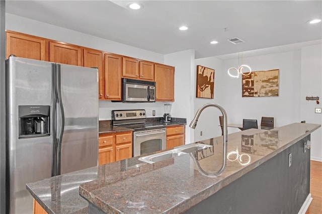 kitchen with dark stone countertops, appliances with stainless steel finishes, sink, and a large island with sink