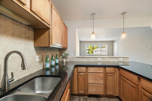 kitchen featuring brown cabinets, hanging light fixtures, decorative backsplash, a sink, and dark stone countertops