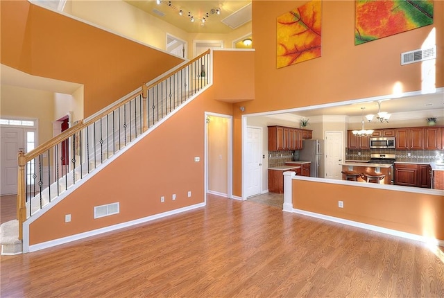 unfurnished living room with light hardwood / wood-style flooring, a chandelier, and a high ceiling