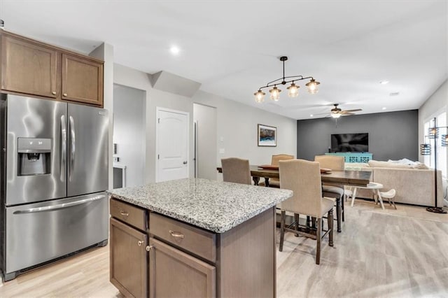 kitchen featuring stainless steel refrigerator with ice dispenser, light stone counters, a kitchen island, decorative light fixtures, and light wood-type flooring