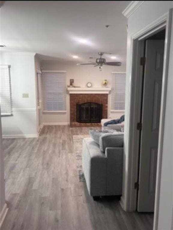 living room featuring a brick fireplace, crown molding, wood-type flooring, and ceiling fan