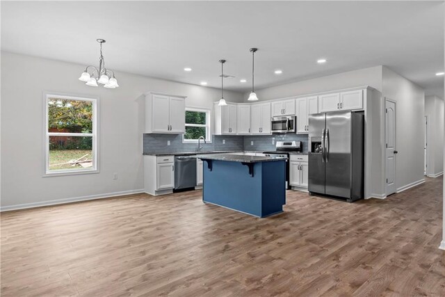 kitchen with a kitchen island, a breakfast bar area, stainless steel appliances, pendant lighting, and white cabinetry