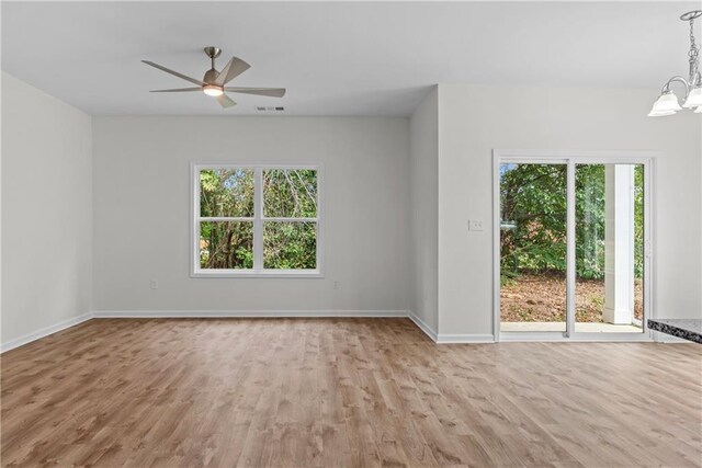 unfurnished room featuring a healthy amount of sunlight, ceiling fan with notable chandelier, and light wood-type flooring