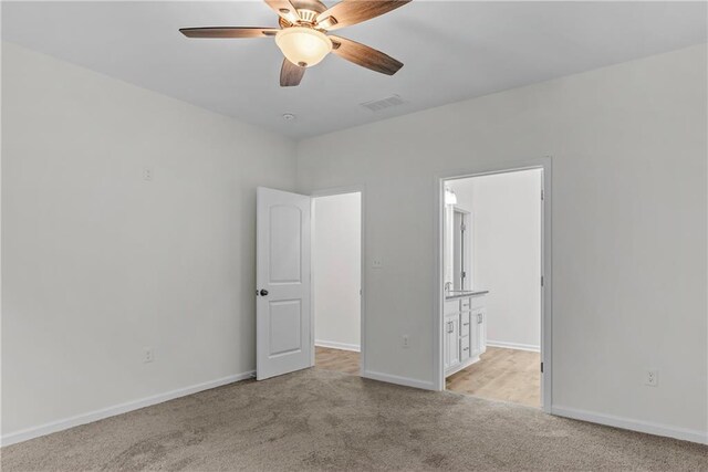 unfurnished bedroom featuring ensuite bath, light colored carpet, and ceiling fan