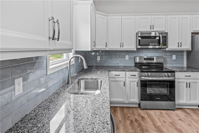 kitchen with tasteful backsplash, appliances with stainless steel finishes, sink, white cabinetry, and light hardwood / wood-style flooring