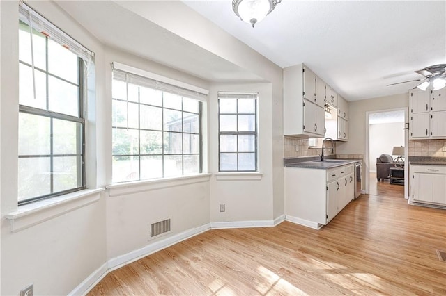 kitchen with tasteful backsplash, light wood-type flooring, visible vents, white cabinetry, and baseboards