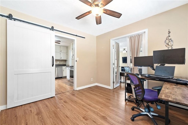 office space featuring a ceiling fan, baseboards, light wood-style flooring, and a barn door
