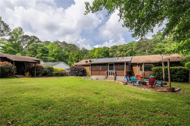 back of property with a sunroom, a yard, and an outdoor fire pit