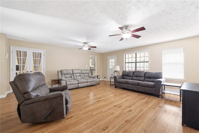living room with light wood-type flooring, baseboards, ceiling fan, and a textured ceiling