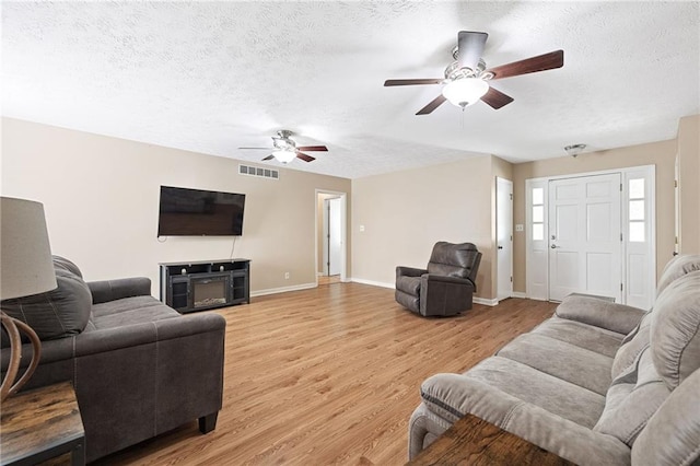 living area with light wood-style flooring, a textured ceiling, baseboards, visible vents, and ceiling fan